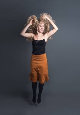 Sarı saçlı genç ve güzel bir dansçı karanlık bir arka plan stüdyosunda zıplıyor.