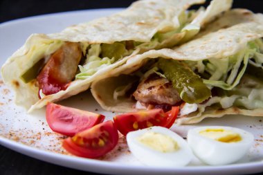 Dilimlenmiş tavuk, salatalık konservesi ve soslu lahana, beyaz tabakta pide ekmeğine sarılmış. Öğle veya akşam yemeği için lezzetli. Pita ekmeğiyle bir tabakta domates ve yumurta parçaları. 