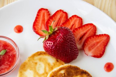 Peynirli, çilekli krep ve ahşap arka planda beyaz bir tabakta sos. Kahvaltı ya da öğle yemeği için lezzetli peynirli krep ve çilek. Meyveli lezzetli yemek..