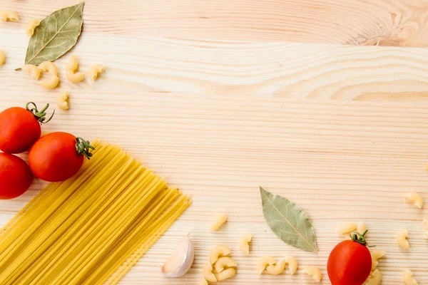Cooking food background with free space for text. Composition with pasta, tomato, eggs, garlic, bay leaf over the wood background. Ingredients for cooking with copy space. Top view with copy space
