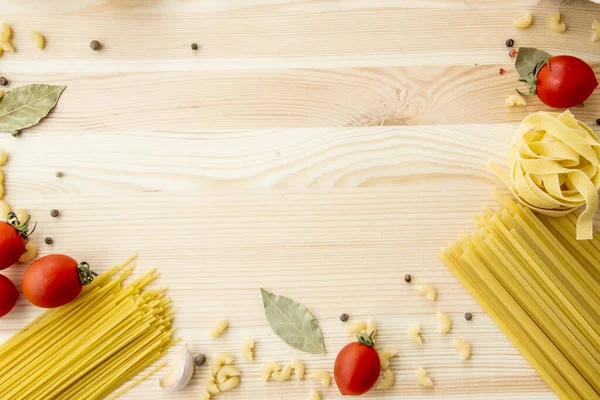 Cooking food background with free space for text. Composition with pasta, tomato, eggs, garlic, bay leaf over the wood background. Ingredients for cooking with copy space. Top view with copy space