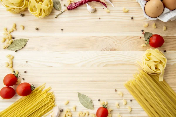 Cooking food background with free space for text. Composition with pasta, tomato, eggs, garlic, bay leaf over the wood background. Ingredients for cooking with copy space. Top view with copy space