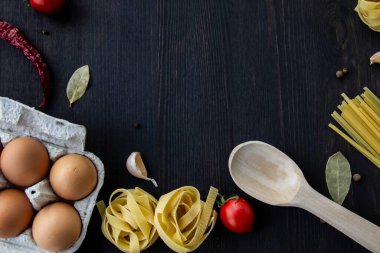 Yemek pişirme arka planında mesaj için boş yer var. Spagetti, domates, yumurta, sarımsak, ahşap arka planda defne yaprağı. Fotokopi alanı ile yemek yapmak için gerekli malzemeler. Tasarım için üst görünüm