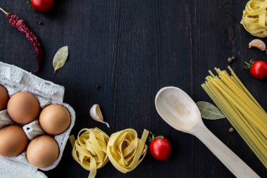 Yemek pişirme arka planında mesaj için boş yer var. Spagetti, domates, yumurta, sarımsak, ahşap arka planda defne yaprağı. Fotokopi alanı ile yemek yapmak için gerekli malzemeler. Tasarım için üst görünüm