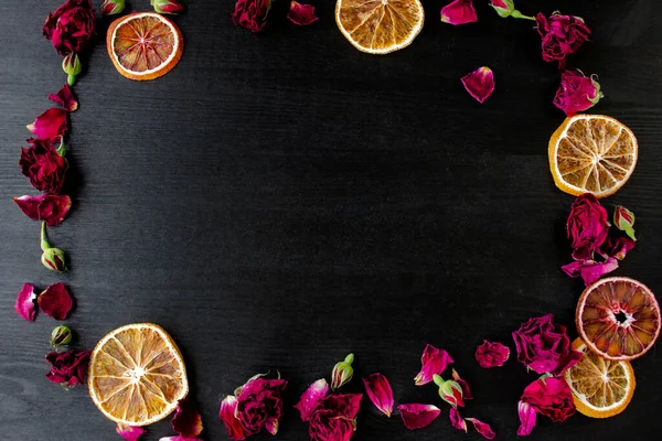 Wooden background with dry roses and petals and slices of dry orange with copy space. Flat lay composition with frame border made of dry roses and citrus.