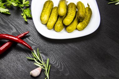 Biber, maydanoz, sarımsak, biberiye, ahşap arka planda beyaz tabakta salatalık turşusu. Yemek pişirme arka planında mesaj için boş yer var. Kopyalama alanı olan üst görünüm