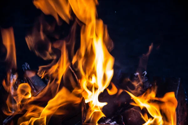 Karanlık bir arka planda yangın. Yakacak odun ateşi. Yanan kıvılcımlar, ateş şekilleri. Karanlıkta kırmızı ve turuncu cehennem ateşi..