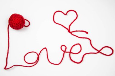 Beyaz arkaplana karşı kırmızı iplik. Kırmızı iplikli kırmızı tüy yumağı beyaza izole edilmiş bir kelime yazar. Kalp ve sözcük Kırmızı iplikle yazılmış aşk.