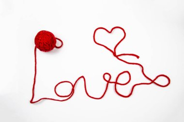 Beyaz arkaplana karşı kırmızı iplik. Kırmızı iplikli kırmızı tüy yumağı beyaza izole edilmiş bir kelime yazar. Kalp ve sözcük Kırmızı iplikle yazılmış aşk.