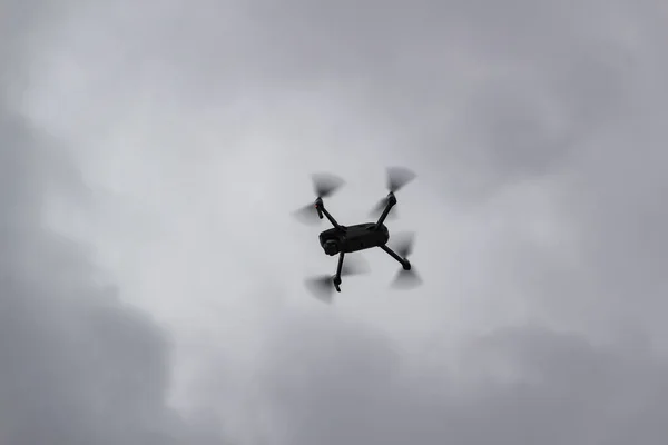 Drone flying in grey sky with clouds in the background. Silhouette of drone flying in cloudy grey sky.