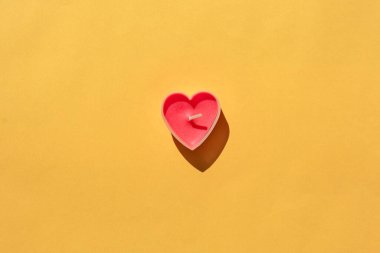 Sarı arka planda kalp şeklinde bir mum. İzole et. etiket için yer