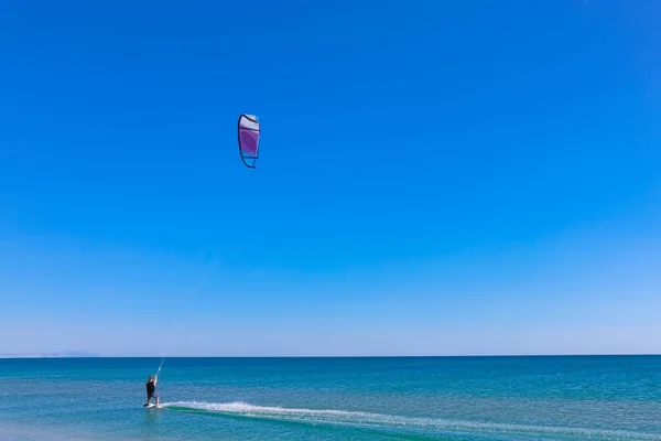 Een kitesurfer die surft op het gladde azuurblauwe water. recreatieve sport. Een man rijdt met een vlieger in het zeewater. Extreme sport. Spring maar. — Stockfoto