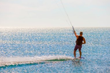 Uçurtma sörfçüsü pürüzsüz gök mavisi sularda sörf yapıyor. Eğlence sporu. Bir adam deniz suyunda uçurtma sörfü yapıyor. Ekstrem. Atla