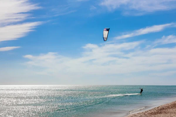 Een kitesurfer die surft op het gladde azuurblauwe water. recreatieve sport. Een man rijdt met een vlieger in het zeewater. Extreme sport. Spring maar. — Stockfoto