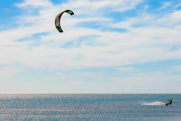 Een kitesurfer die surft op het gladde azuurblauwe water. recreatieve sport. Een man rijdt met een vlieger in het zeewater. Extreme sport. Spring maar. — Stockfoto