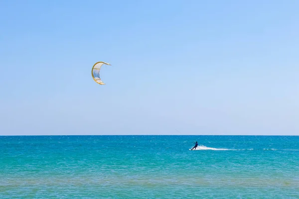Een kitesurfer die surft op het gladde azuurblauwe water. recreatieve sport. Een man rijdt met een vlieger in het zeewater. Extreme sport. Spring maar. — Stockfoto