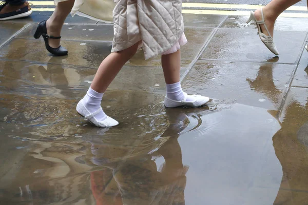 A well-dressed girl in white shoes goes from school through the puddle after heavy rain