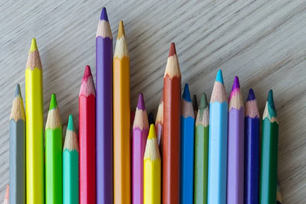 The group of a different length colored drawing pencils are laying on the wooden desk background and waiting for a painting lesson.