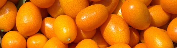 Ferske, saftige kumquater i en kurv på markedet. Oransje bakgrunn av ferske appelsiner. Avslutning – stockfoto