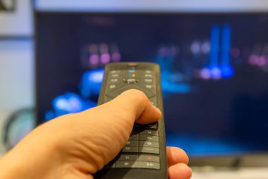 el ile bir televizyon TV uzaktan kumanda arka planda tutarak. yakın çekim