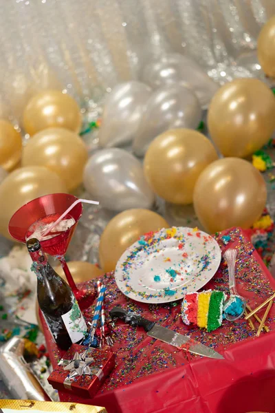 The mess after the party. Balloons in white and gold, plate with cake crumbs and empty bottle of wine.
