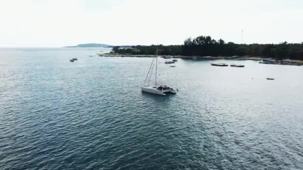 Vista aérea de um iate catamarã ancorado de pé e as pessoas podem tomar sol em seu convés . — Vídeo de Stock