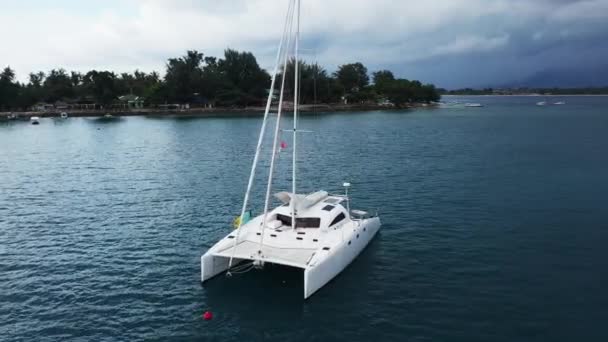 Vista aérea de um iate catamarã ancorado de pé e as pessoas podem tomar sol em seu convés . — Vídeo de Stock