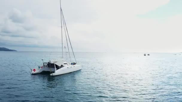 Vista aérea de um iate catamarã ancorado de pé e as pessoas podem tomar sol em seu convés . — Vídeo de Stock