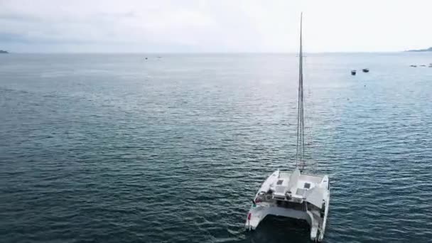 Luftaufnahme einer vor Anker liegenden Katamaran-Jacht, auf deren Deck sich die Menschen sonnen können. — Stockvideo