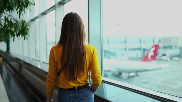 在机场终端窗口附近电话讲话的年轻欧洲妇女在错过飞行以后心烦和沮丧. — 图库视频影像