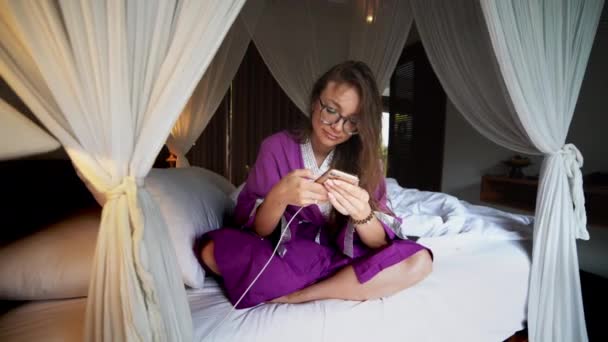 Krásná žena, která používá telefon v posteli a spravuje chytré připojení domů s mobilní aplikací — Stock video