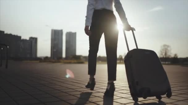 Business lady gonna taxi parkeren van de luchthaven met haar bagage. Meisje in hakken intensivering en roll koffer op wielen. Vrouw met haar koffer langs straat wandelen. Travel concept. Slow motion — Stockvideo