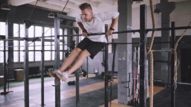 Gövdesi fit ve elleri güçlü beyaz erkek sporcu dışarıda barfiks çekiyor. Yakışıklı sarışın sporcu stadyum yatay barına yanaşıyor. Metin ol bar egzersizleri..