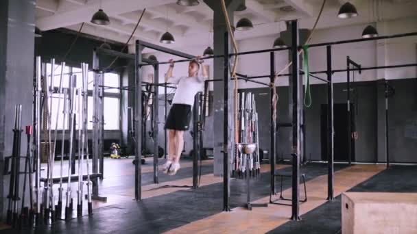 Hombre se detiene en la barra en el gimnasio, lleva equipo de elevación y agarre y camiseta blanca — Vídeo de stock