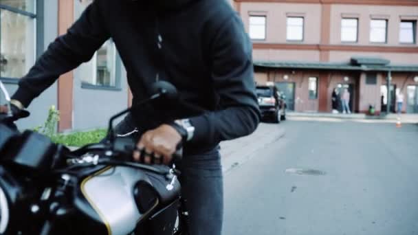 Biker in leather gloves and black hoodie starts motorcycle. — Stock Video