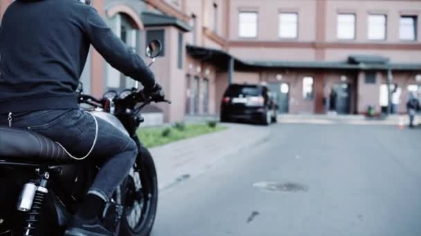 Motorradfahrer in schwarzem Kapuzenpulli und Lederhandschuhen kommt und stellt Motorrad ab. — Stockvideo
