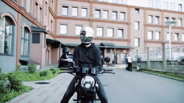 Young man and biker in helmets on motorcycle in city with urban background. — Stock Video