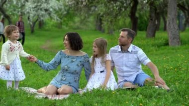 Anne, baba ve sevimli kızları çocuklar çiçek açan ağaç bahçesinde ekose rahatlayın