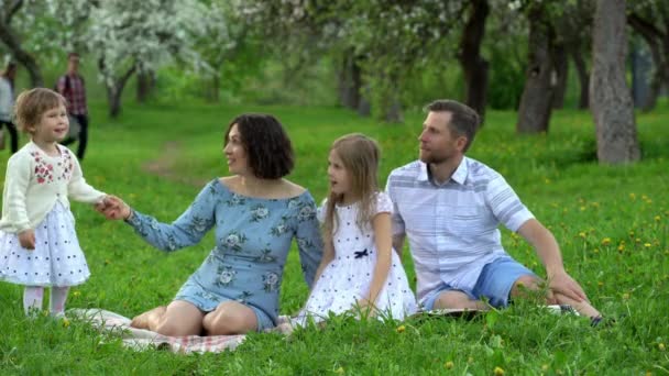 Moeder, vader en schattige dochters kinderen ontspannen op Plaid in bloeiende boomtuin — Stockvideo