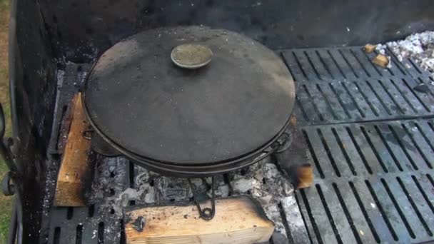 Voedsel bereiden in pot op rooster. Rook stijgt uit kolen. Handheld schot — Stockvideo