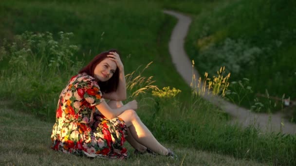 公園の草原の草原に座っている幸せな若い女性。静的ショット — ストック動画