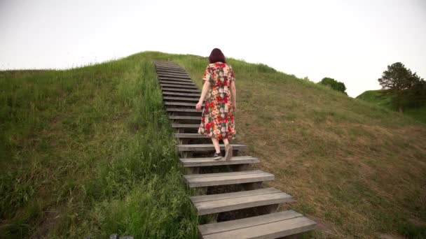 Femme en robe colorée monter sur un monticule d'escalier en bois. Plan statique — Video