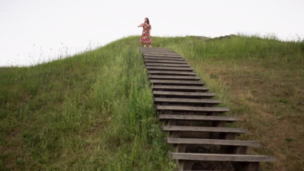 Ahşap merdivenlerile höyük tepenin üstüne bakan oyuncu kız — Stok video