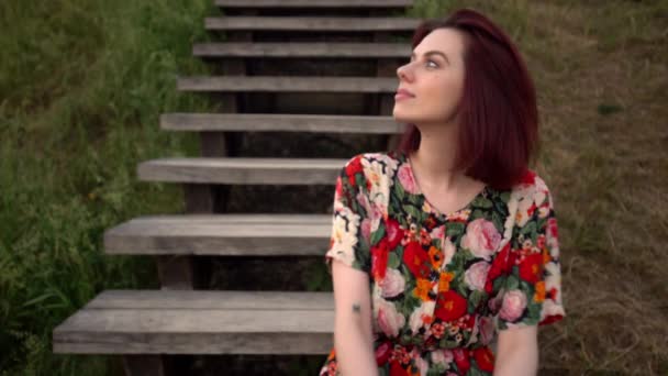 Mladá krásná zrzavá žena sedí na dřevěných schodech v parku — Stock video