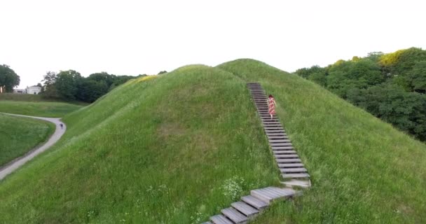 Woman in dress climb up on wooden stairs hill. Aerial drone shot. — 비디오