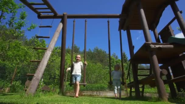 Naughty kids brother and sister run away from swing on playground. Handheld — Stock Video