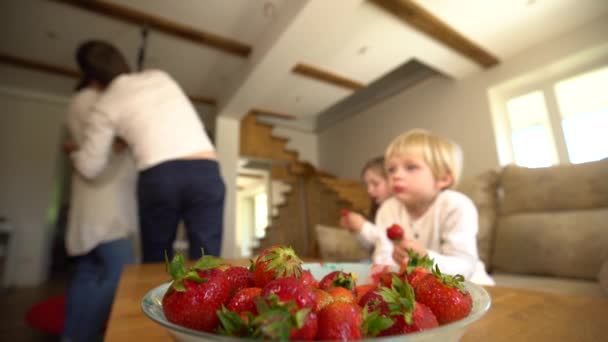 Чаша, полная спелых клубники и размытых членов семьи едят ягоды. Портативный — стоковое видео
