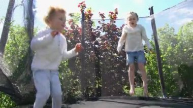 Erkek ve kız evin arka bahçesinde trambolin üzerinde atlama. El çekimi