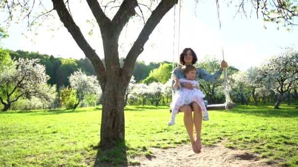 Young woman swinging on wooden swing with little pretty girl in dress. Static — Stock Video