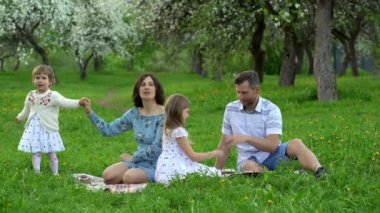 İki kızı olan genç ebeveynler baharda parktaki bir ekose üzerinde boş vakitlerini geçirirler.